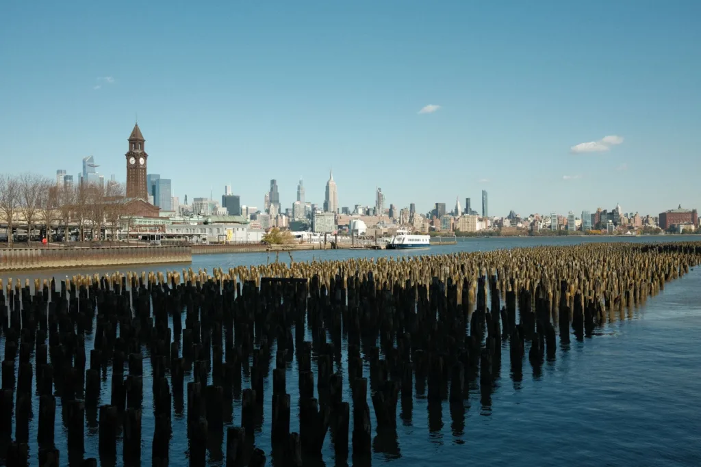 Old pier pilings on the Hudson River with a clock tower and the Manhattan skyline in the distance