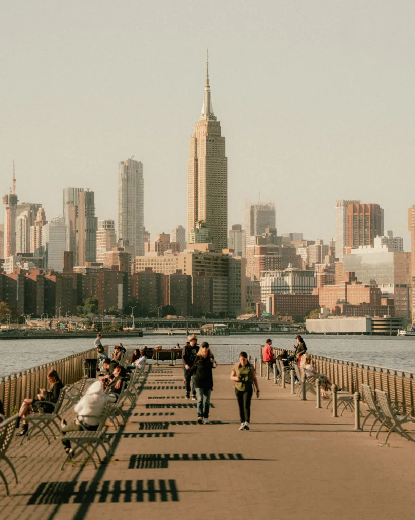 People on a waterfront pier with the Empire State Building and Midtown Manhattan skyline behind