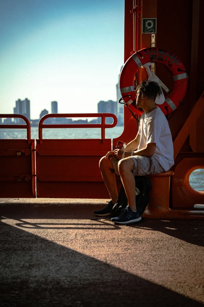 Young man sitting on the deck of the Staten Island Ferry with the city skyline behind