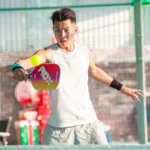 A player hits a forehand volley with a pink paddle on a fenced pickleball court