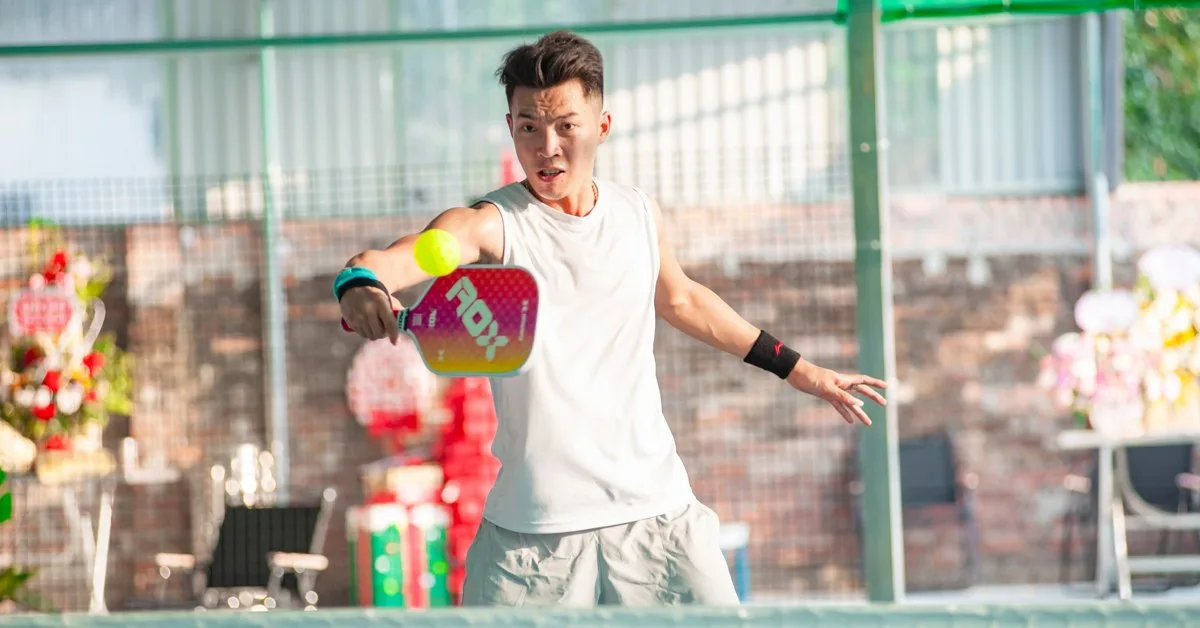 A player hits a forehand volley with a pink paddle on a fenced pickleball court