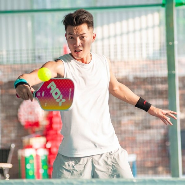 A player hits a forehand volley with a pink paddle on a fenced pickleball court
